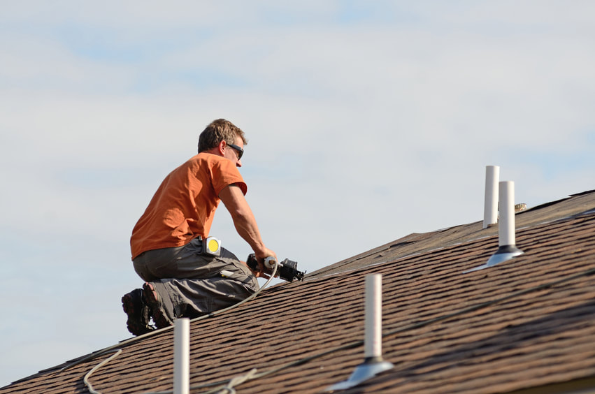Photograph of roofer using nail gun to attach shingle to a new roof